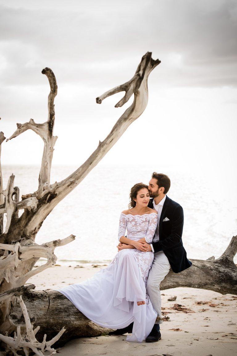 A gorgeous bride and groom sitting on driftwood on a Florida beach, photo by Anna Nguyen of Zee Anna Photography